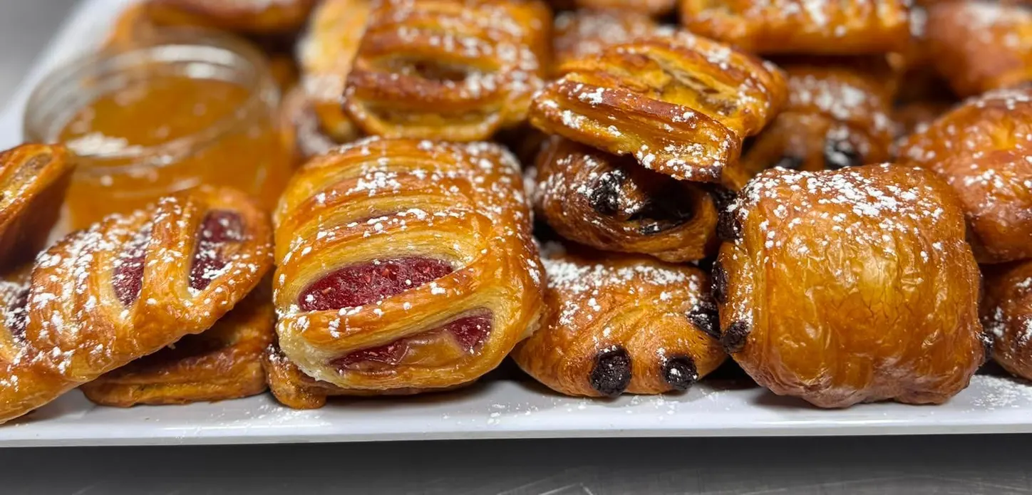 Freshly baked breakfast pastries dusted with icing sugar, with preserves